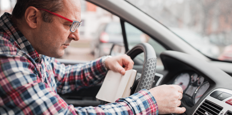 man in vehicle recording odometer, evoking manual mileage reporting