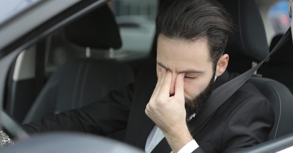 man driving vehicle pinching nose in emotion evoking driver insurance compliance