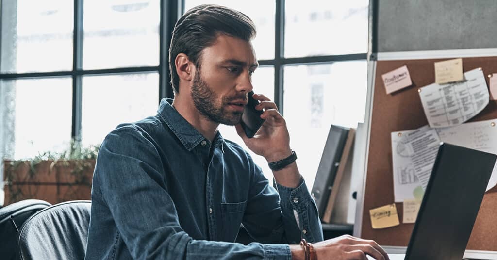 man working from home using phone and laptop evoking implement byo program